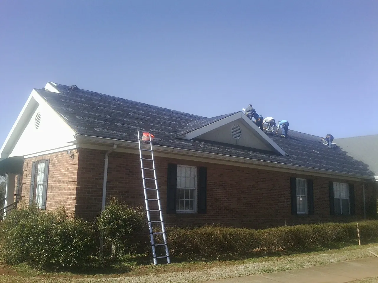 Crew tearing shingles off a brick ranch roof with a ladder set — Metal Roof Repair work by our crew in East Bend