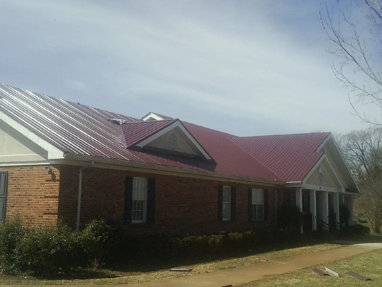 Red metal roof with gabled entries on a long brick building, from a Hail Damage Roof Repair job in East Bend