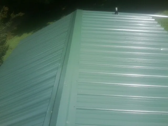 New green metal panels meeting at the ridge of a roof — Flat Roof Repair work by our crew in East Bend