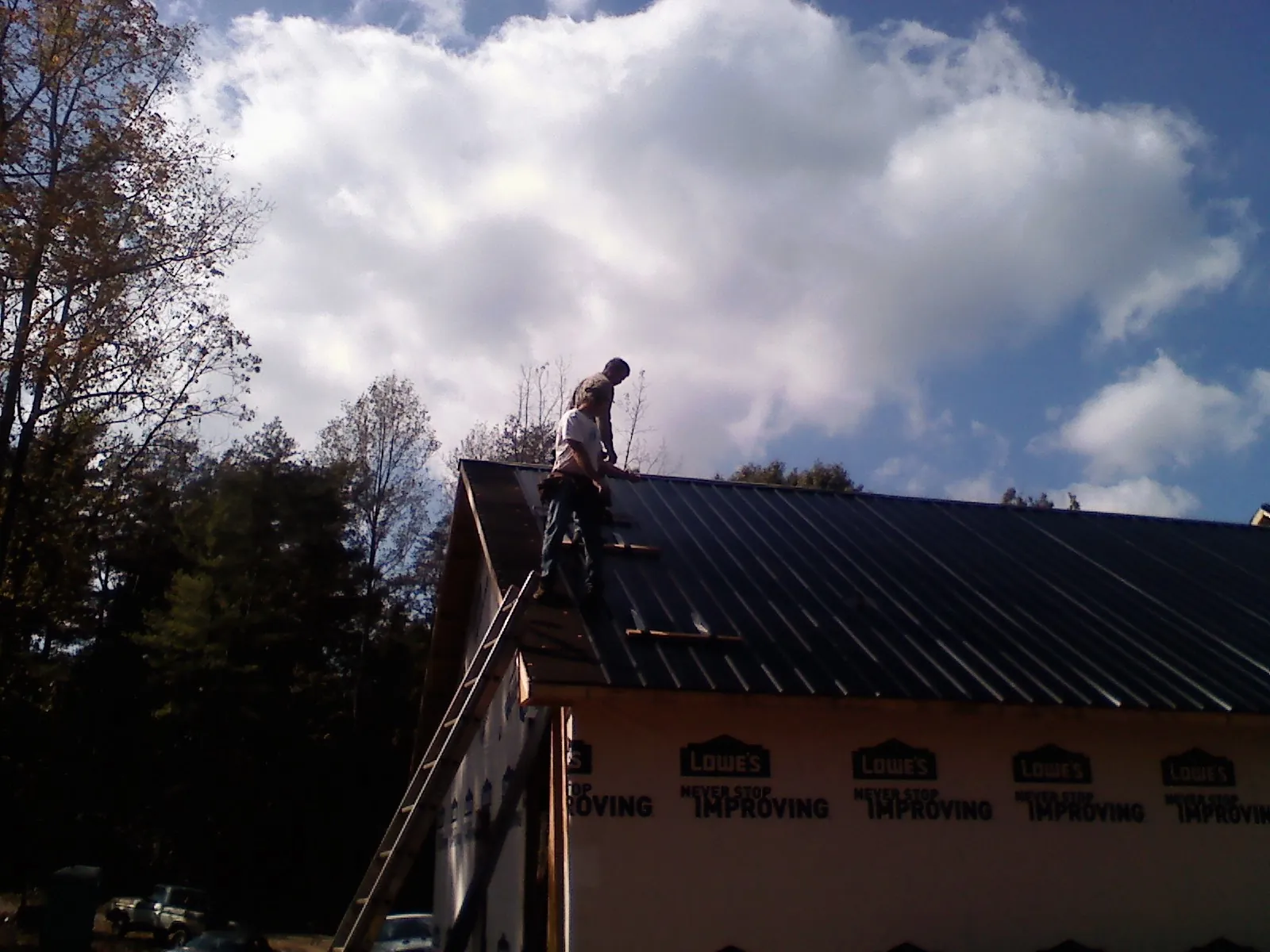 Roofer fastening dark metal panels high against a cloudy sky, from a Roof Inspection job in East Bend