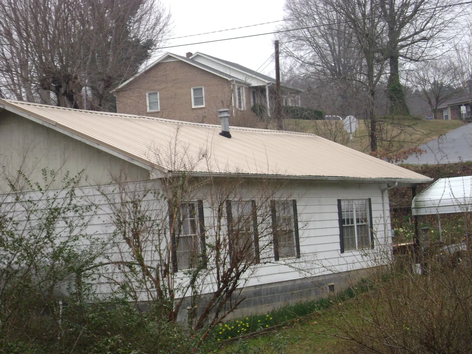 Tan metal roof on a white sided house set into a hillside — Commercial Roofing by Roofing Brothers in East Bend